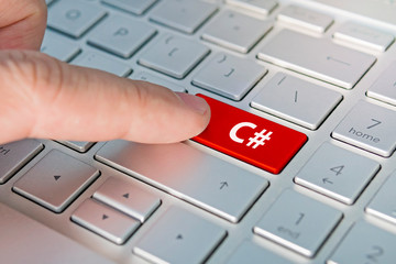 C computer language. The writing on button modern of gray laptop. Finger presses the button. Programmer for work.