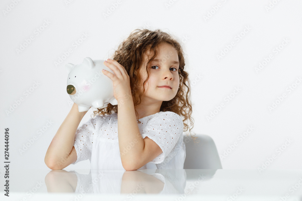 Frontal portrait of a cute curly girl in white holding a piggy bank ...