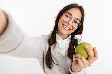 Sticker - Happy young school girl isolated over white wall background posing take a selfie by camera eat apple.