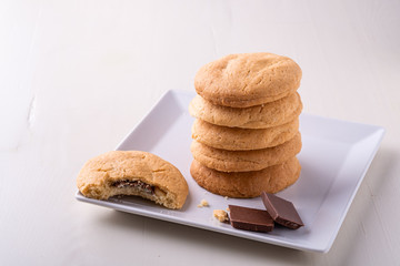 Homemade stack of shortbread chocolate cookies with one bitten cookie and two pieces of chocolate on white plate wooden table