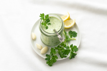 Yoghurt cilantro sauce with garlic and olive oil in a glass jar on a white background, selective focus