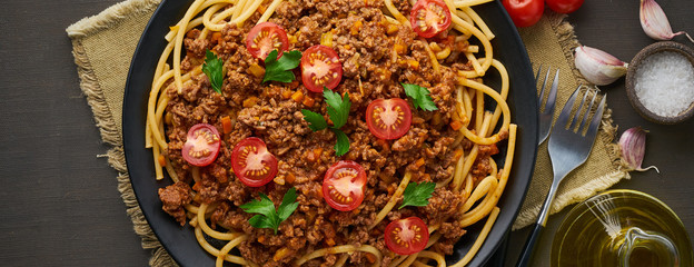 Wall Mural - Pasta Bolognese bucatini with mincemeat and tomatoes, dark wooden background, top view, banner long