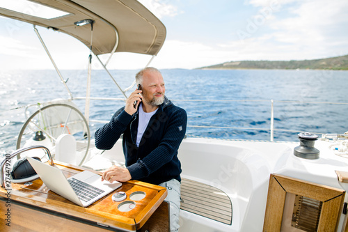 Cuadros en Lienzo Digitaler Nomade mit Laptop telefoniert mit Blick in die Ferne auf einem Segelbo