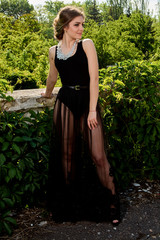 Young attractive woman in the sexy see-through, transparent, transpicuous, diaphanous, clear black dress posing at summer sunny day outdoor in the old park. Fashion woman. Young woman modern portrait.