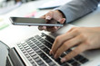 © Bojan - Close up of female hand holding smart phone and typing on laptop keyboard.
