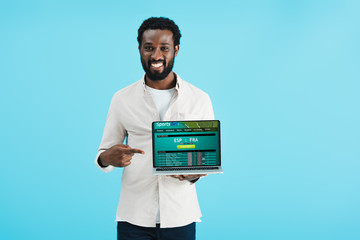 smiling african american man pointing at laptop with sports bet website isolated on blue