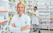 © Karanov images - Portrait of a female pharmacist, male colleague working with drugs in the background.