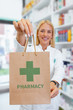 © Karanov images - Pharmacist holding paper bag with a green Pharmacy logo in a drugstore