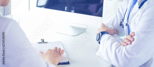 Cuadros en Lienzo Handsome doctor is talking with young female patient and making notes while sitt