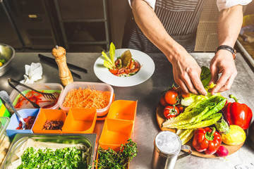 Professional chef cooking in the kitchen restaurant at the hotel, preparing dinner. A cook in an apron makes a salad of vegetables and pizza.