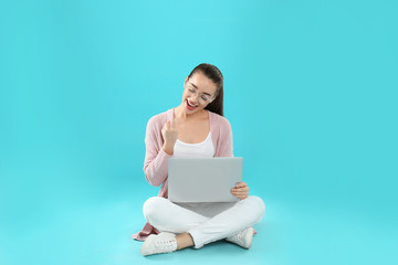 Poster - Happy young woman in casual outfit with laptop sitting on color background