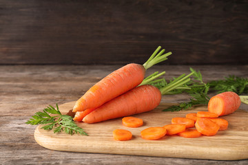 Board with cut carrot on wooden background