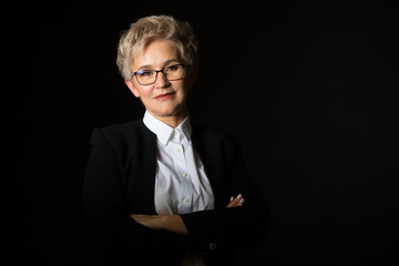 stylish elderly woman in glasses and black jacket on a black background	