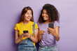 © wayhome.studio - Positive millennial mixed race sisters pose with modern smartphone devices, addicted to technologies, chat online, Afro American woman shows photos to friend on cellular, points into screen.