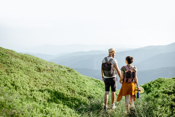 beautiful couple walking with backpacks on the green meadow, while traveling high in the mountains d