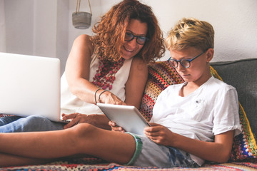 Beautiful teen reading new trend stories online on tablet with mum. Technology addicted young boy watching social video at home with his mother. Child and mommy communicate and plays with tech device.