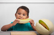 A child eating a slice of fresh honeymelon fruit on his own and enjoying a healthy alternative to processed foods.