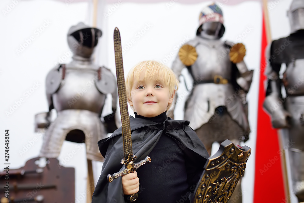 Portrait of a cute little boy dressed as a medieval knight with a sword ...