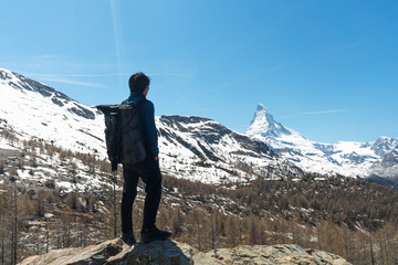 Wall Mural - travelling in switzerland, a man with backpack standing on the rock looking at matterhorn mountain v