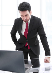 Wall Mural - Businessman standing at his Desk and looking at the laptop screen