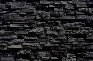 dark anthracite gray, almost black texture of a wall made of horizontal slim cut stone blocks.