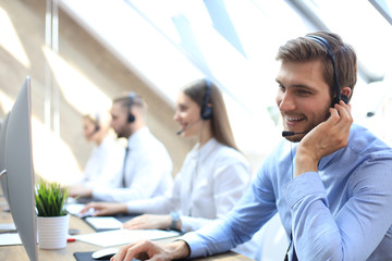 Wall Mural - Portrait of call center worker accompanied by his team. Smiling customer support operator at work.