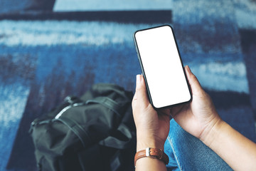 Wall Mural - Mockup image of a woman's hands holding and using black mobile phone with blank screen while sitting in the airport