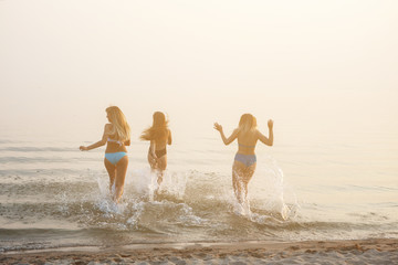 Canvas Print - Three beautiful young women running to the sea.