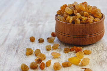 Sticker - Light yellow raisins in a wooden bowl on a light white background. Close-up. Isolated.