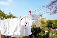 Rack dryer standing on the terrace on sunny day for drying white clothes. Collapsible clotheshorse with clothes plastic pegs bag. Plastic basket for clothespins. copy space