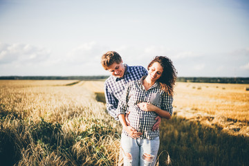 A happy couple enjoying time in the countryside. Man and woman smiling and resting on the field. Pregnant happy woman. 