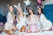 © Тарас Нагирняк - Young women wearing pajamas and bunny ears together at home sitting on bed holding balloons sending air kiss to camera smiling playful..