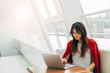 © Anton - Calm and peaceful young woman working at table near window. Type on keyboard of laptop. Alone in room. Wear stylish red jacket. Productive day.