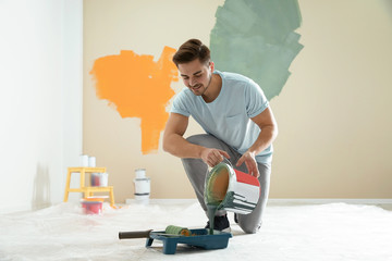 Canvas Print - Young man pouring paint from bucket into tray indoors. Home repair