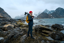 Young Man Photographer Standing At Rock In The Mountains At Beach Photographing The Landscapes On Lofoten Islands In Norway.