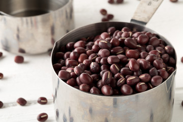 Wall Mural - Raw, uncooked, dried adzuki (red mung) beans in metal measurement cups on white wooden table background