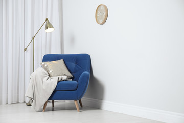 Stylish armchair with pillow and plaid near white wall, space for text. Interior design