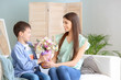 © Pixel-Shot - Little son greeting his mother with bouquet of flowers at home