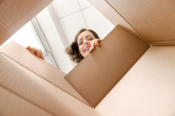 young woman opening parcel at home, view from inside of box