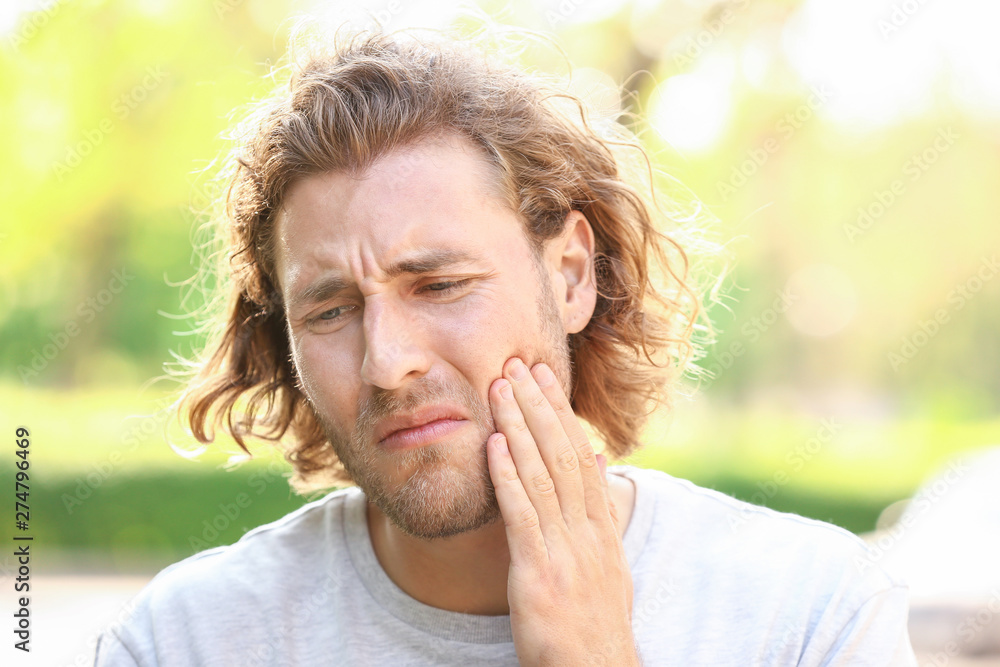 Young man suffering from toothache outdoors