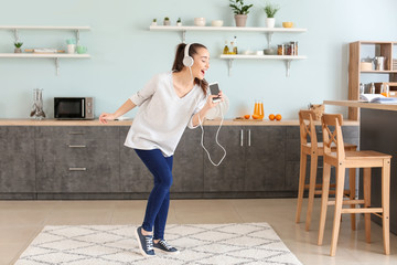 Sticker - Beautiful woman listening to music in kitchen at home