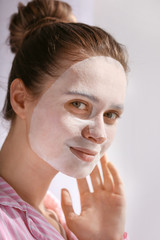 Wall Mural - Young woman with sheet facial mask on light background