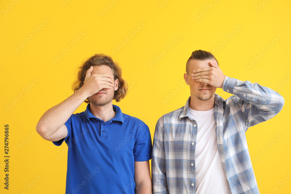 Young men covering their eyes on color background