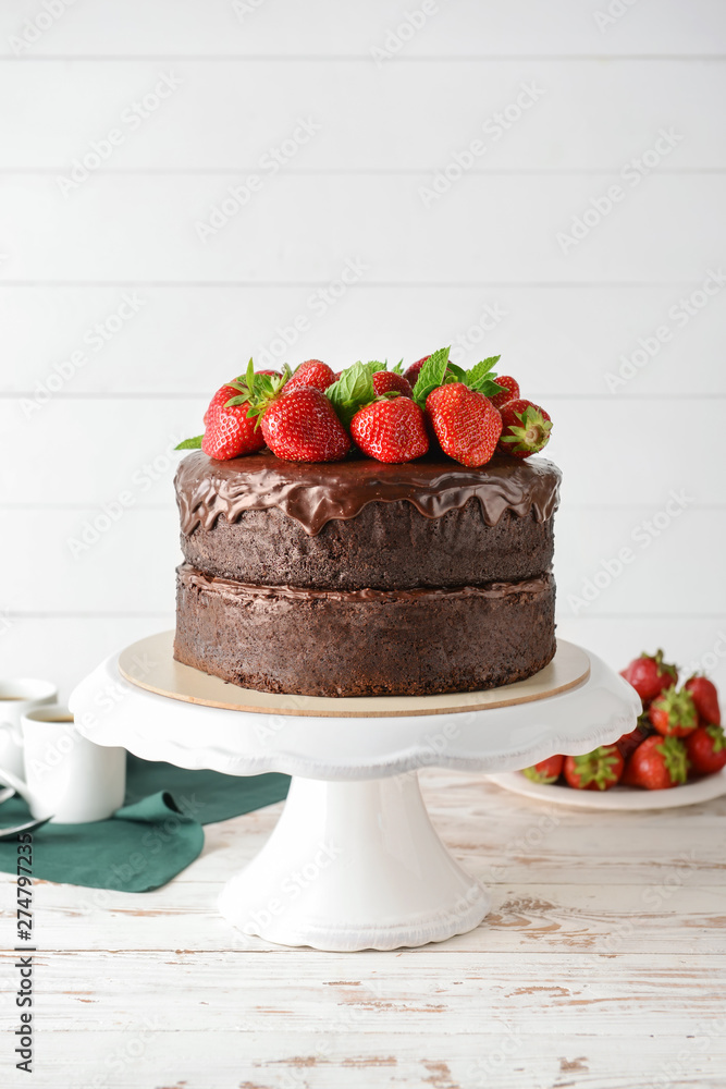 Stand with tasty chocolate cake on white wooden table