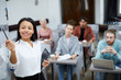 © Seventyfour - Waist up portrait of smiling businesswoman pointing at whiteboard while presenting training course for students in class, copy space