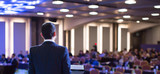 Fototapeta  - Speaker giving a talk at a corporate business conference. Audience in hall with presenter in front of presentation screen. Corporate executive giving speech during business and entrepreneur seminar.