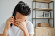© DragonImages - Stressful emotional young man covering eyes when talking on phone with coworker or relative