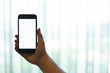 © iHaMoo - hand using a mobile phone with white blank screen against white curtain background