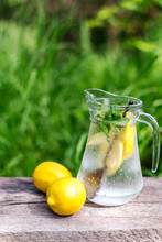 Fresh Lemonade And Two Lemons On Wooden Old Table Against A Green Grass Background