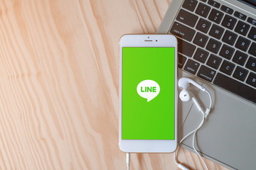 Rayong, Thailand, May 19, 2019: Line logo on smartphone screen placed on laptop keyboard on wood background with earphones and copy space